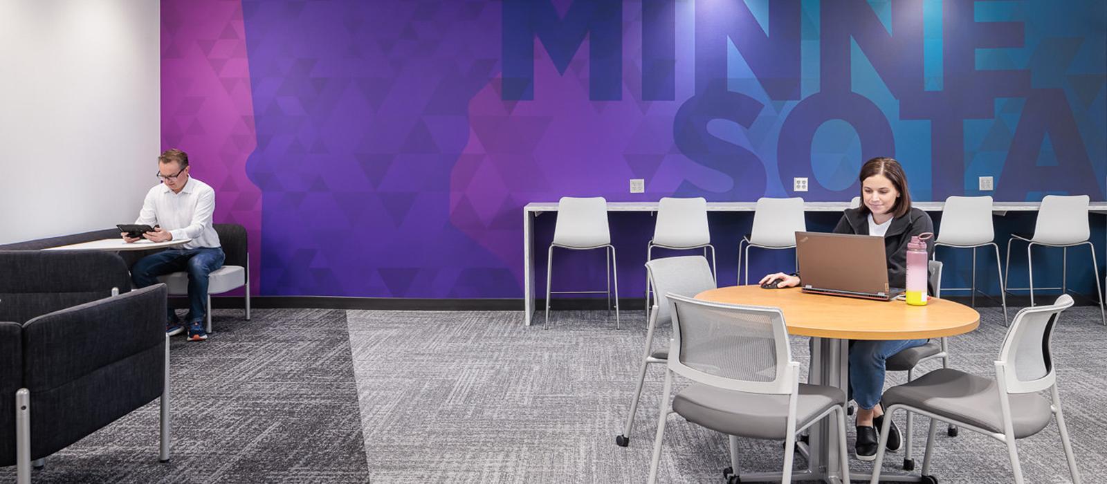 A woman sits at a table studying in front of a Minnesota graphic in the Management Education Center. 