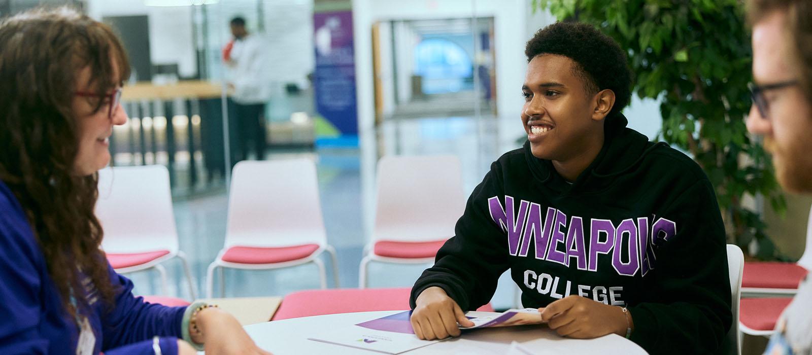 A student holding brochures smiles at an admissions counselor. 