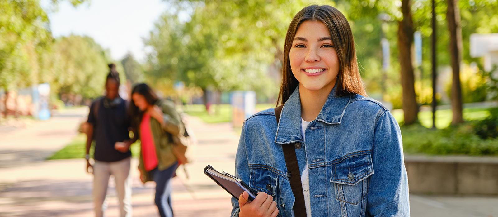 A happy student holding a notebook and standing outside. 