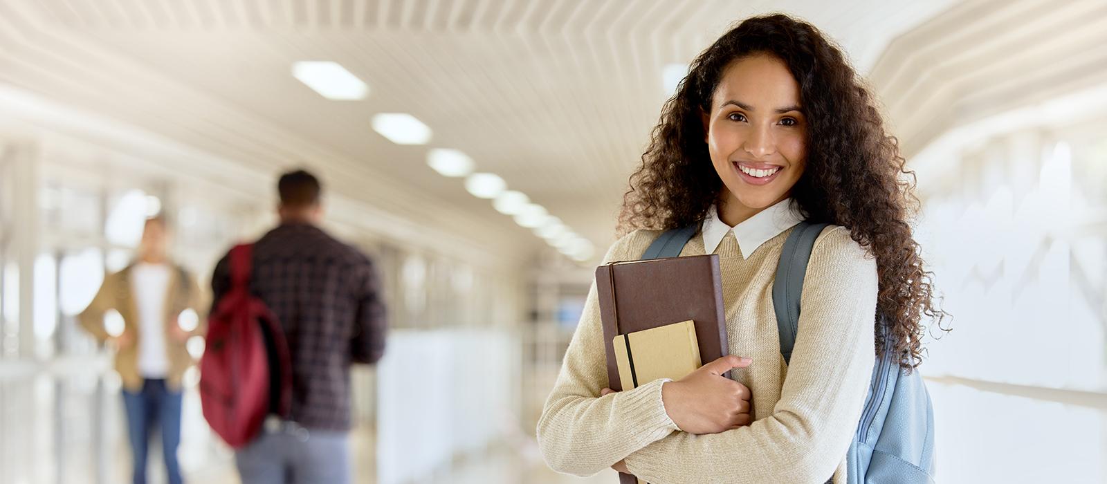 Female student with books and backpack smiling. 