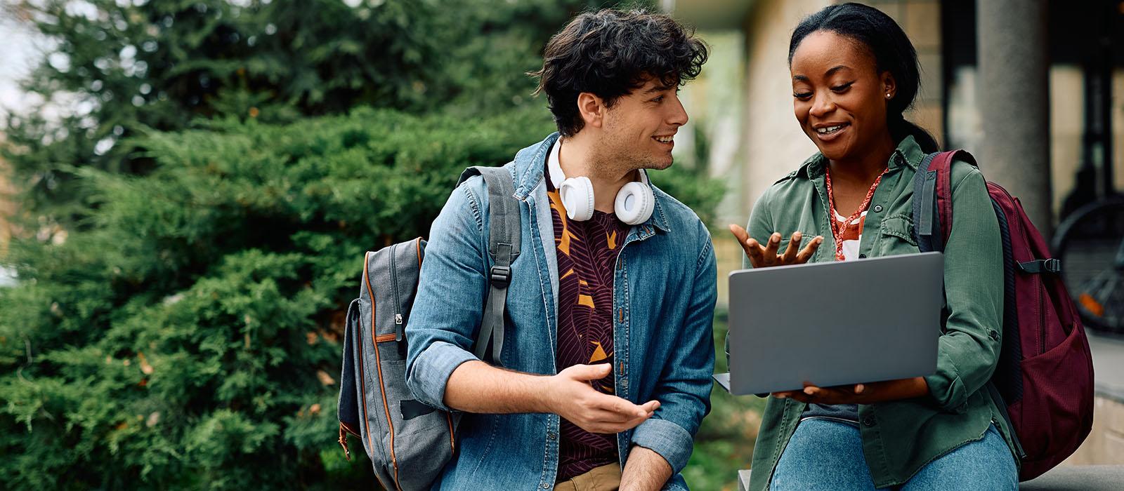 Two students outside in summer talking, smiling. 