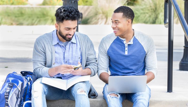 Two students sitting on steps interacting and laughing. 