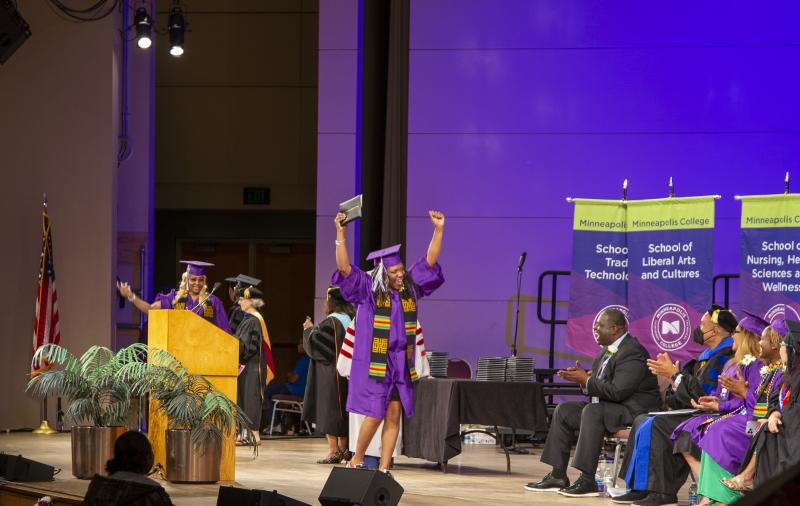 Graduate with arms in the air, walking across stage
