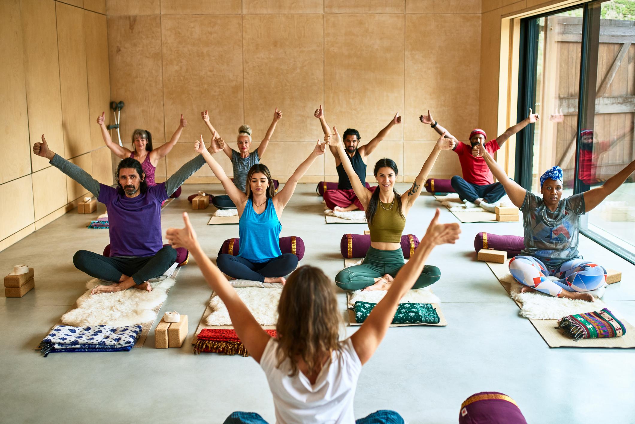Yoga students sitting on mats with arms raised in a yoga class
