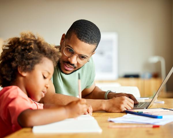 A student parent is sitting at a table studying with their child. 