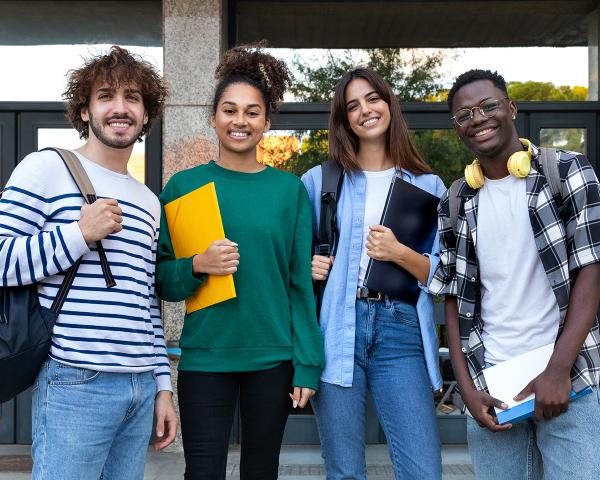 Four smiling students standing in front of a campus building. 