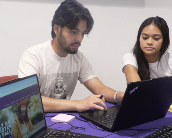 Two students look at a laptop with another laptop in the scene