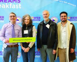 Four people stand together and smile for the camera in front of a step-and-repeat that says Power of Dreams