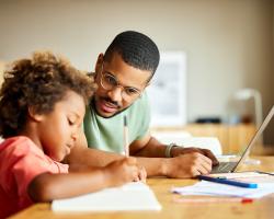 A student parent is sitting at a table studying with their child. 