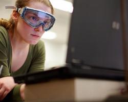 Chemistry Student Studying Assignment in Class student with goggles studying assignment on laptop