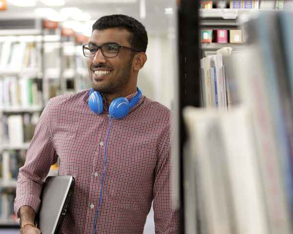 Student in library. leaning against a shelf, smiling.