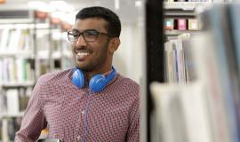 International Student Student in library. leaning against a shelf, smiling.