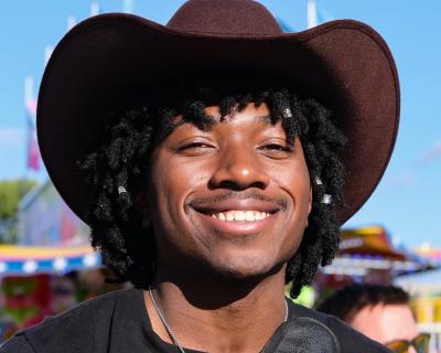 A portrait of Om Harris wearing a cowboy hat while attending the State Fair.