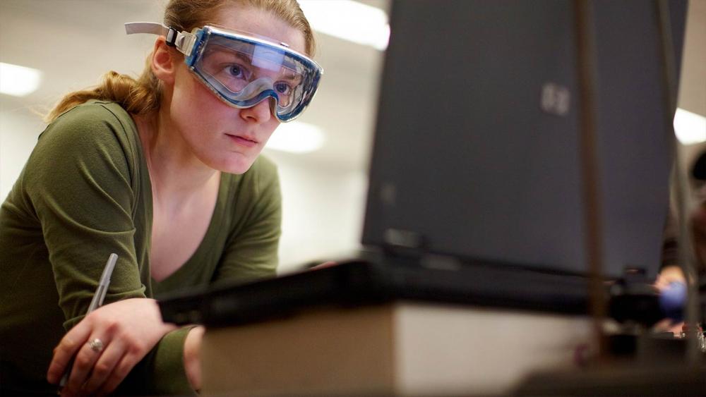 Chemistry Student Studying Assignment in Class student with goggles studying assignment on laptop