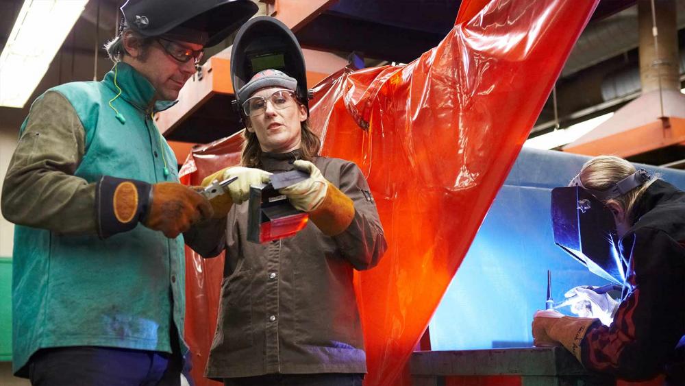 Welding Program at Minneapolis College instructor showing student welding solution with student working in the background